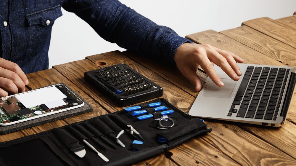 unrecognizable-man-uses-laptop-find-guides-how-repair-electronic-device-tool-bag-broken-gadget-near-vintage-wooden-table Apple accelerates use of recycled materials across all its products